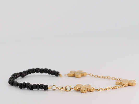 Black beaded bracelet and gold chain bracelet on a light gray background
