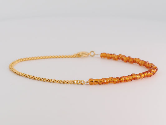 Bracelet with gold chain and orange beads on a light gray background