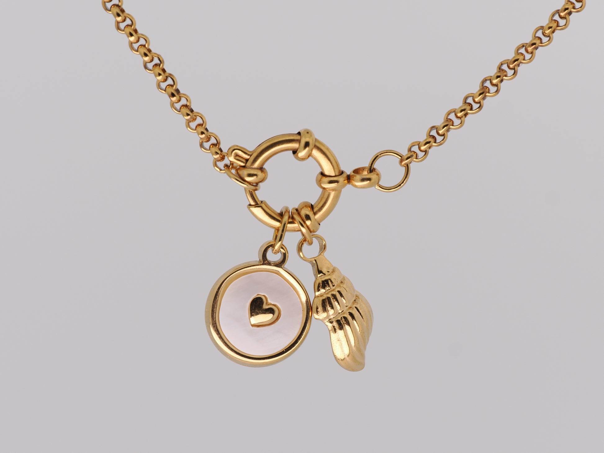 Gold necklace with heart and shell charms on a light gray background