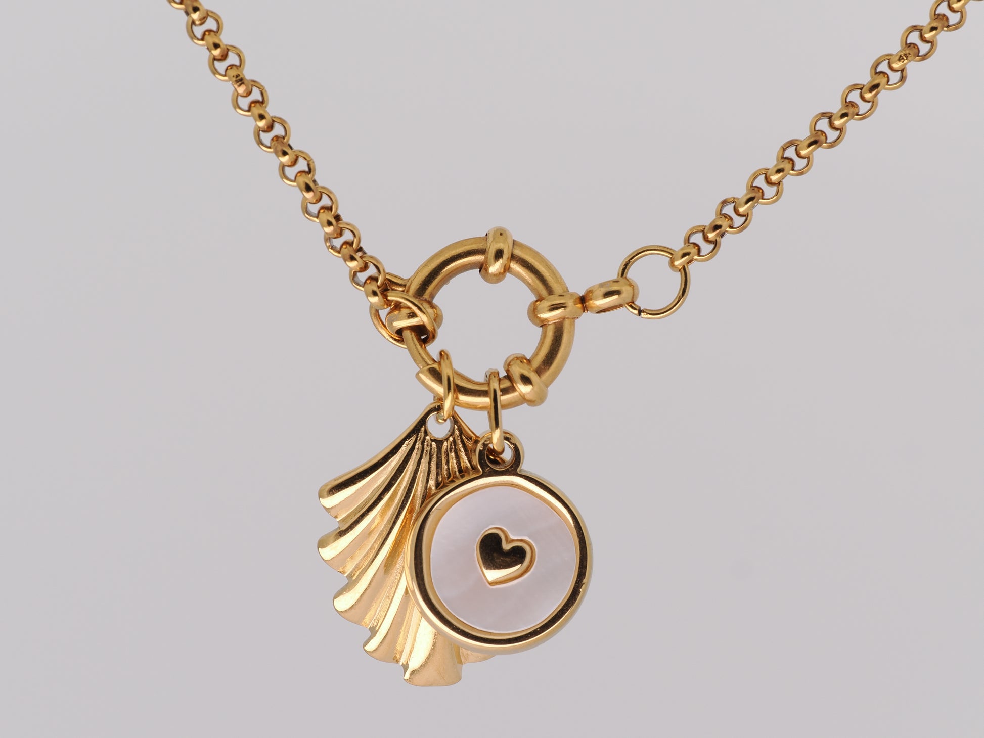 Gold necklace with a scallop shell and heart pendant on a gray background