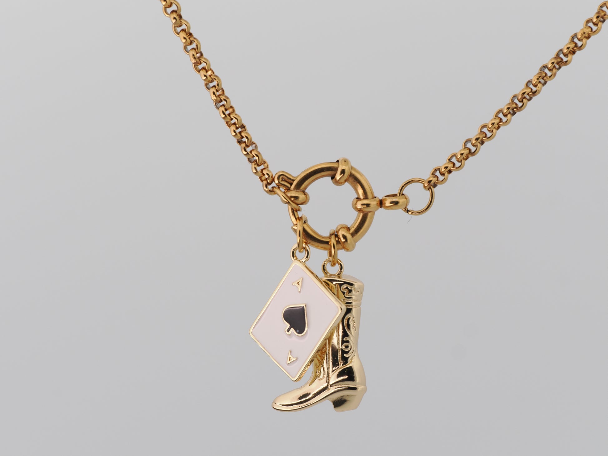 Gold necklace with a spade card and cowboy boot charm on a gray background