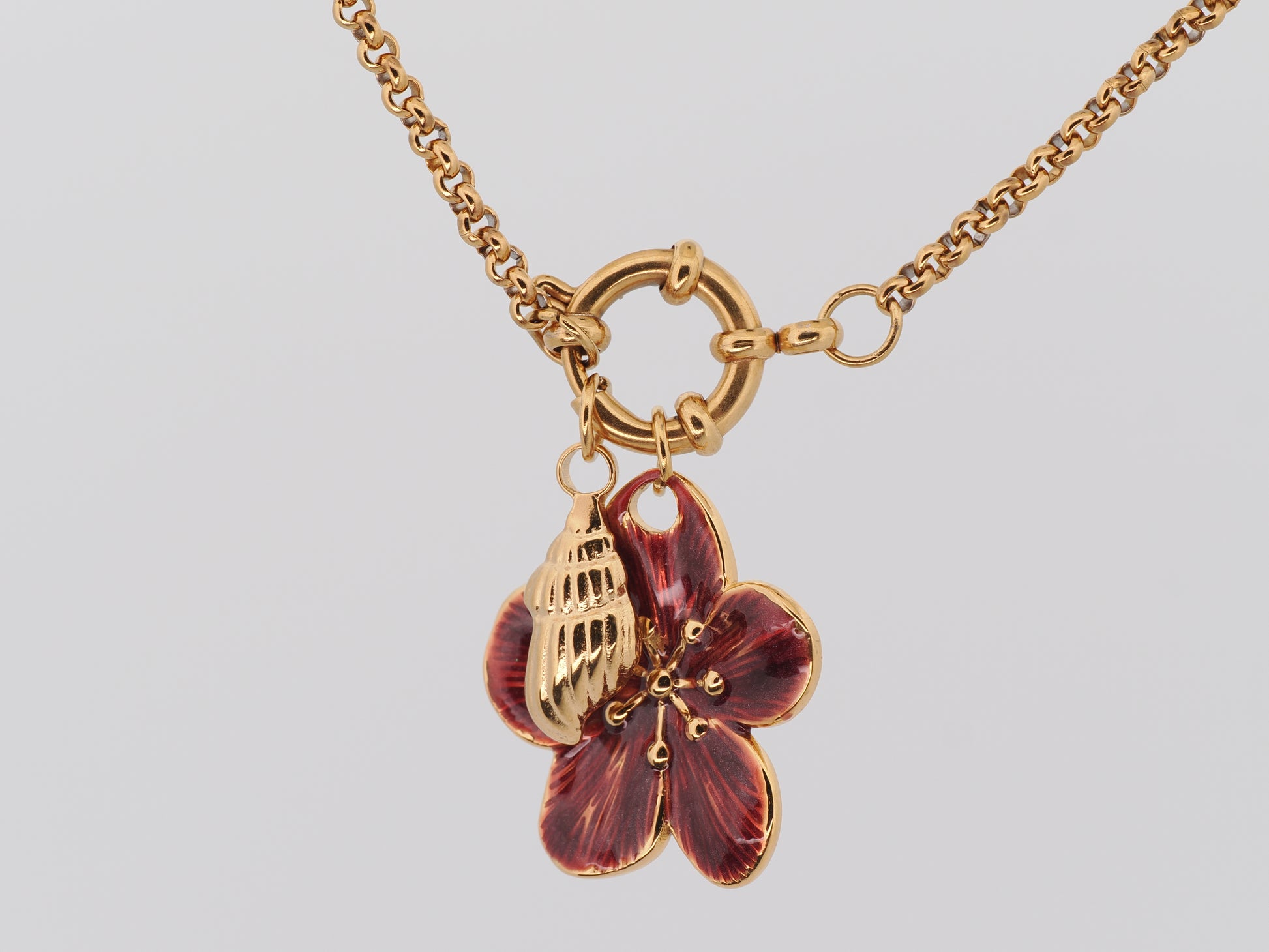 Gold necklace with a red flower pendant on a light gray background