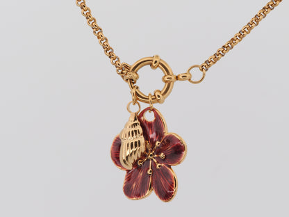 Gold necklace with a red flower pendant on a light gray background