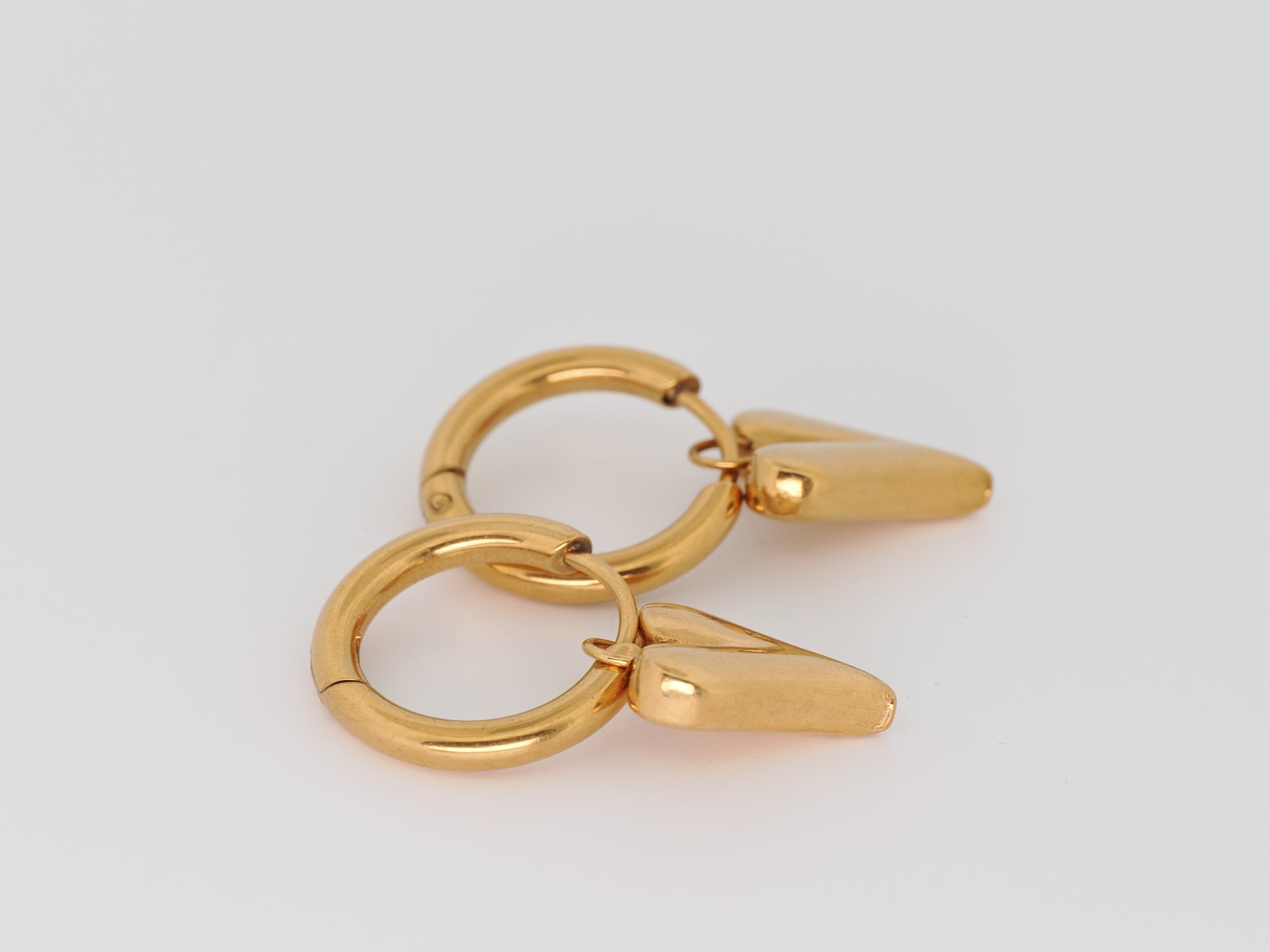 Gold hoop earring with a small triangle-shaped pendant on a light gray background