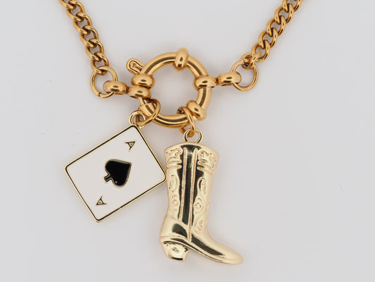 Gold necklace with playing card and cowboy boot charm on a white background