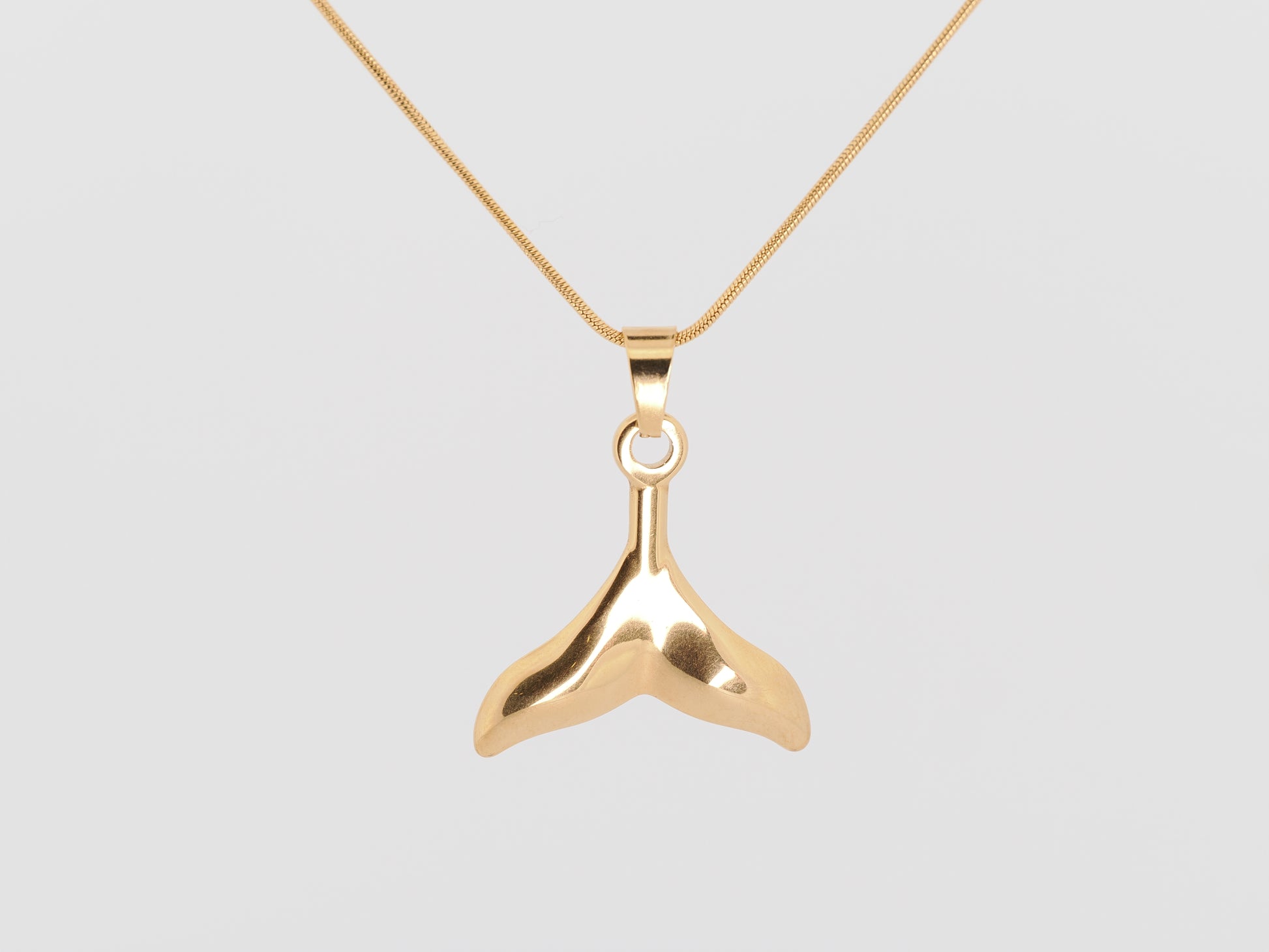 Gold whale tail pendant on a gold chain against a light gray background