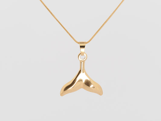 Gold whale tail pendant on a gold chain against a light gray background