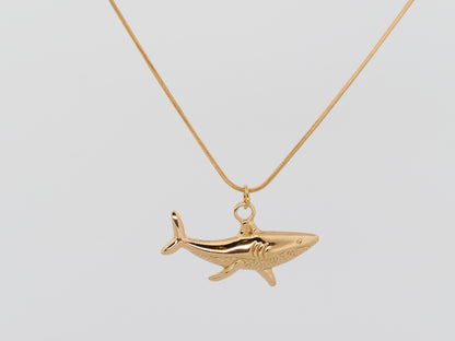 Gold shark pendant on a gold chain against a light gray background