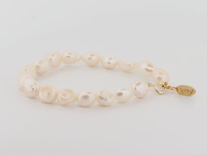 Pearl bracelet with a gold clasp on a light gray background