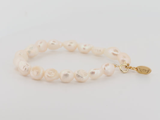 Pearl bracelet with a gold clasp on a light gray background