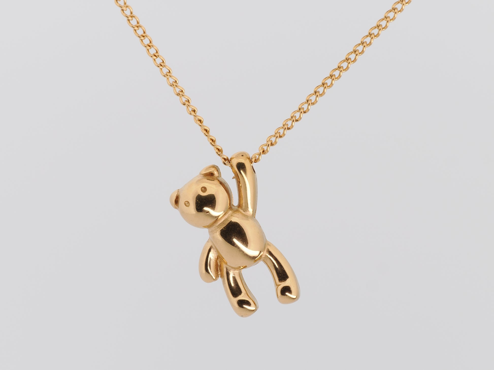 Gold teddy bear pendant on a chain against a light gray background