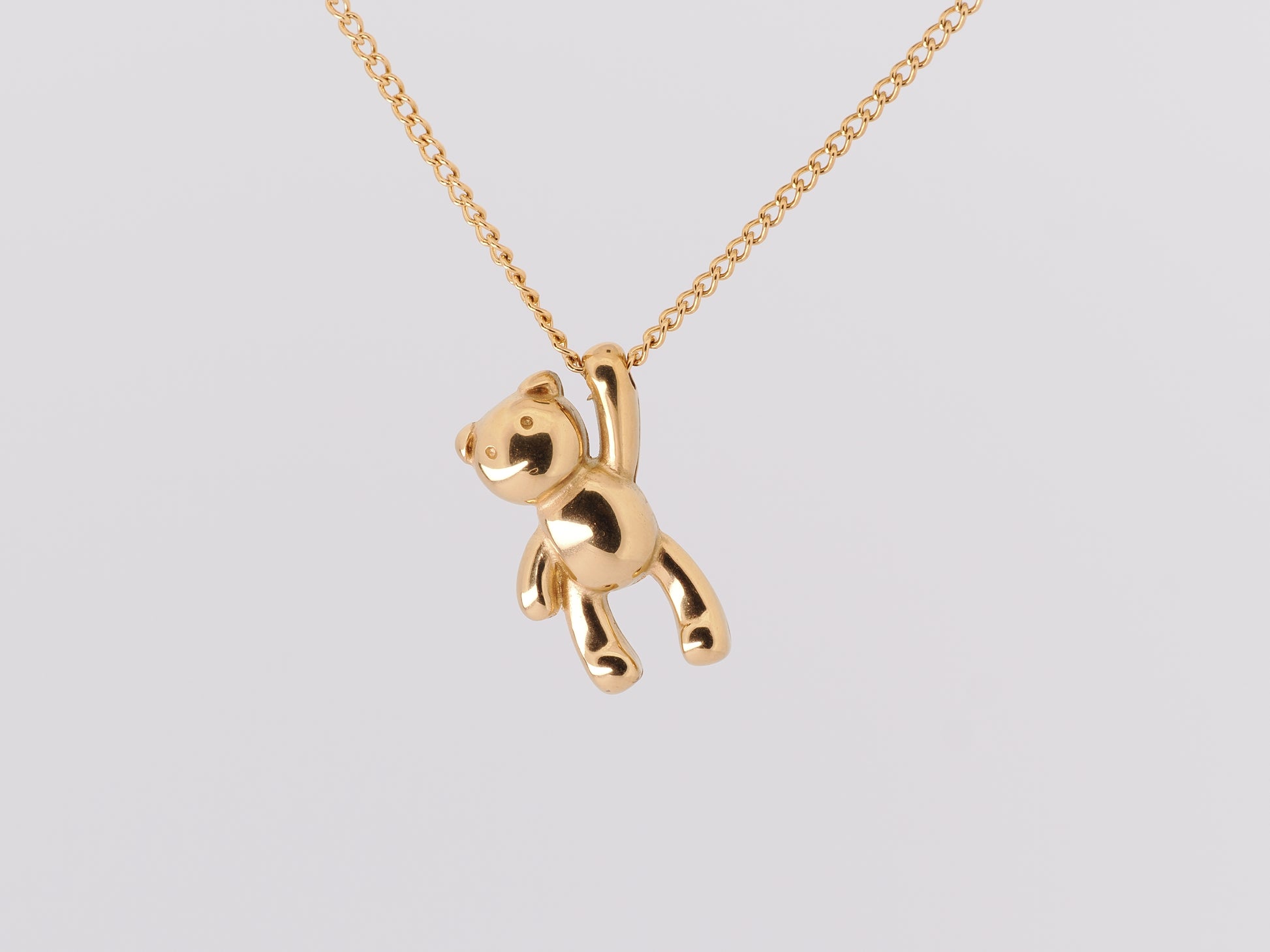 Gold teddy bear pendant on a chain against a light gray background