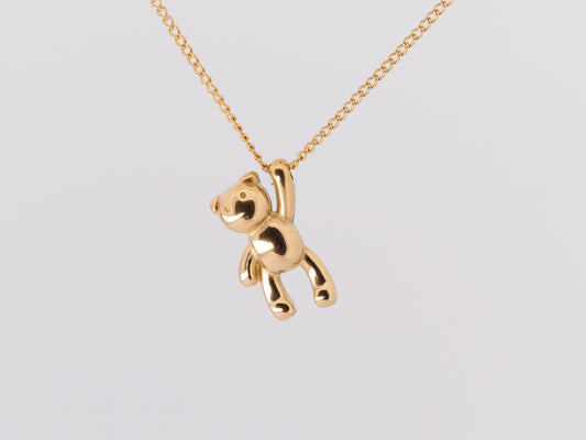 Gold teddy bear pendant on a chain against a light gray background