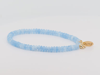 Blue beaded bracelet with a gold charm on a light gray background