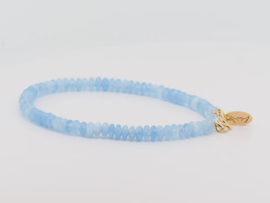 Blue beaded bracelet with a gold charm on a light gray background