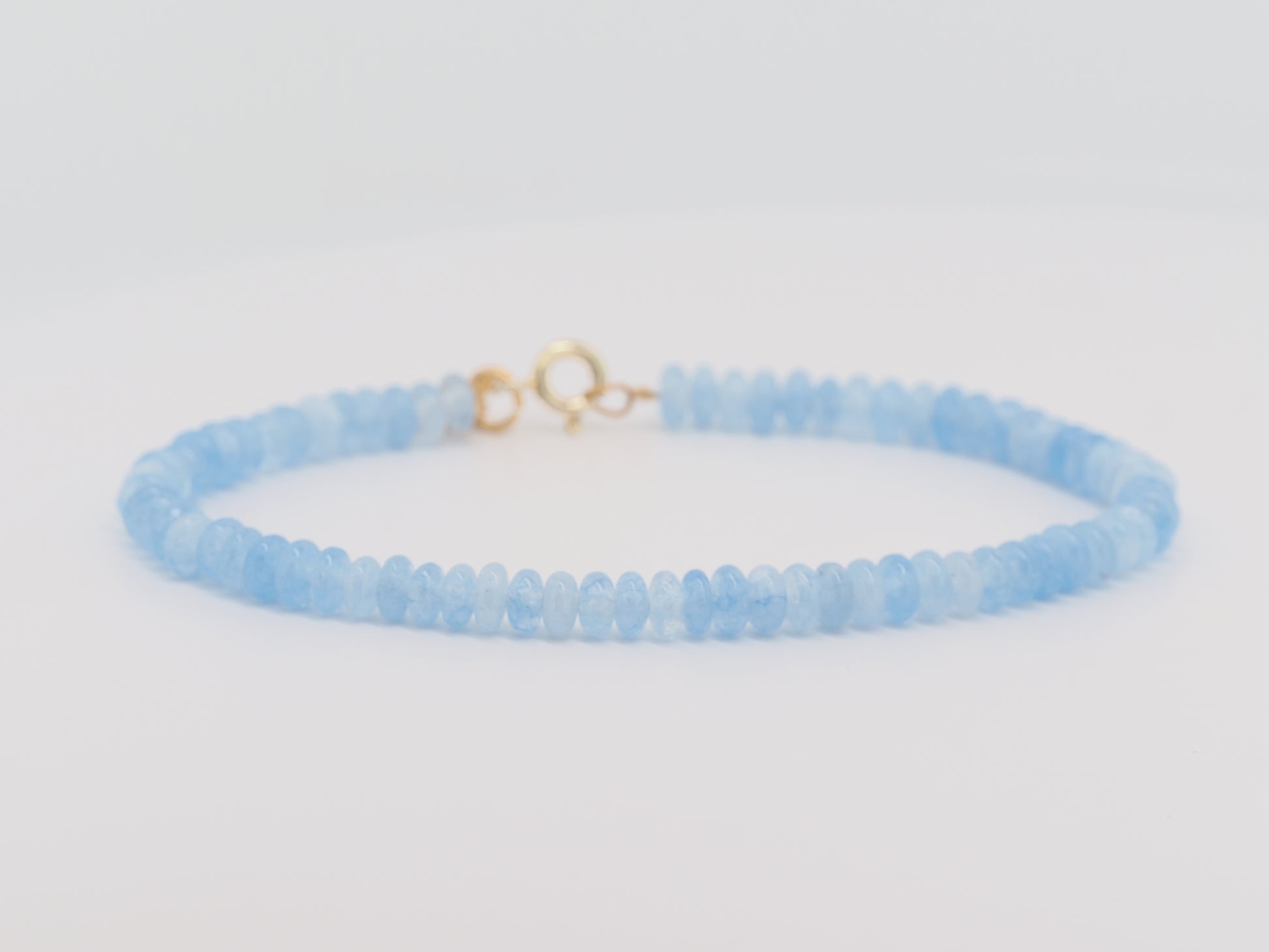 Light blue beaded bracelet with a gold clasp on a light gray background