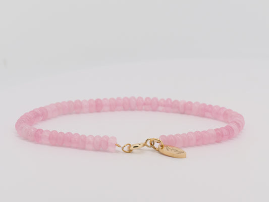 Pink beaded bracelet with a gold charm on a light gray background