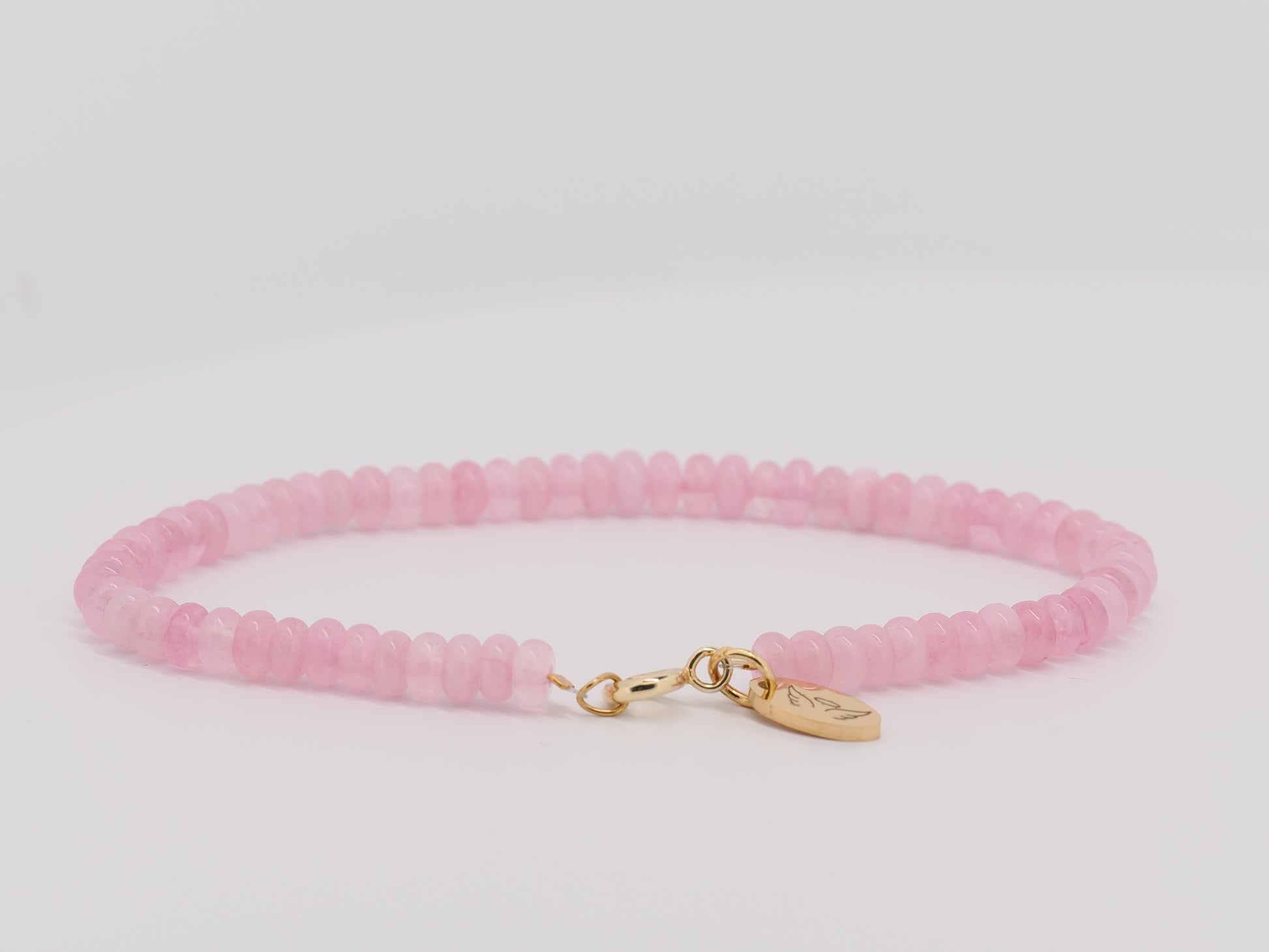 Pink beaded bracelet with a gold clasp on a light gray background