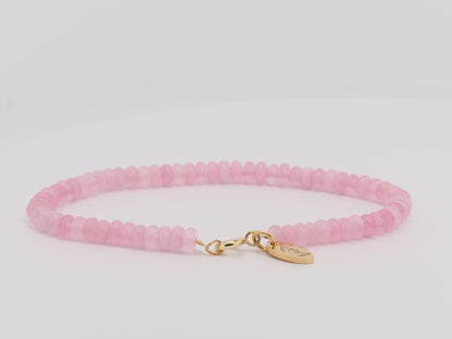 Pink beaded bracelet with a gold clasp on a light gray background