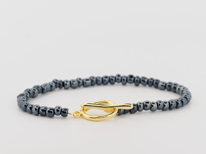 Gray beaded bracelet with a gold clasp on a light gray background