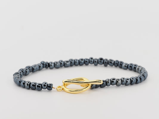 Gray beaded bracelet with a gold clasp on a light gray background