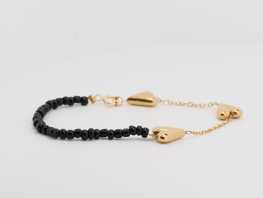 Bracelet with black beads and gold heart-shaped clasps on a light gray background